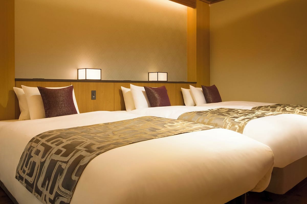 A hotel room with two beds, a wooden headboard, and two wall-mounted lamps.