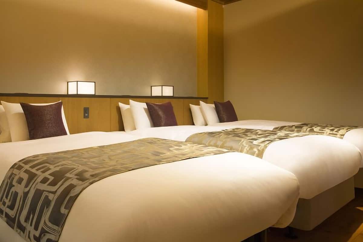 A hotel room with two beds, a wooden headboard, and two wall-mounted lamps.