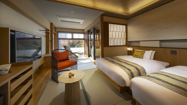 A hotel room with two beds, a TV, a seating area with a chair, and a view of the outside. - onomichi-hansei (Onomichi)