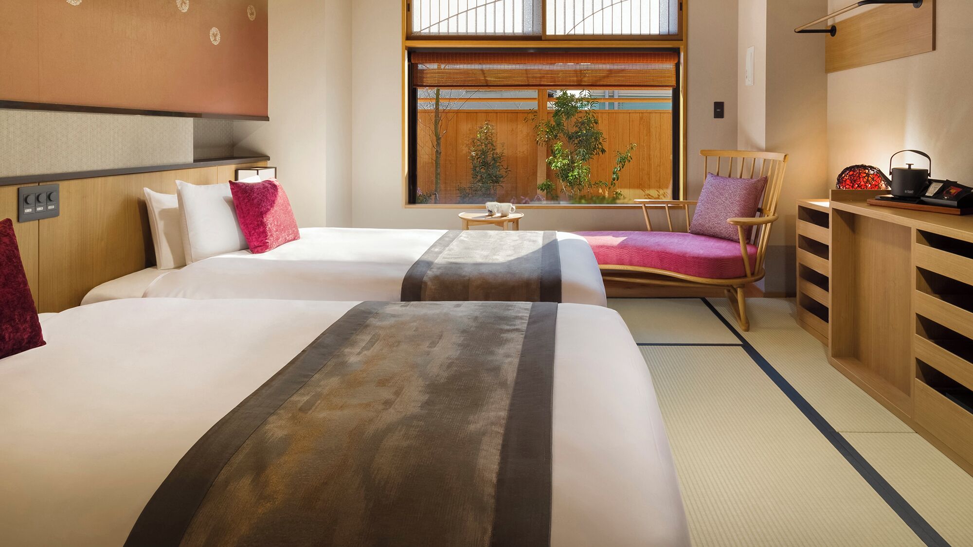 A hotel room with two beds, a wooden chair, a small table, and a view of the outside.