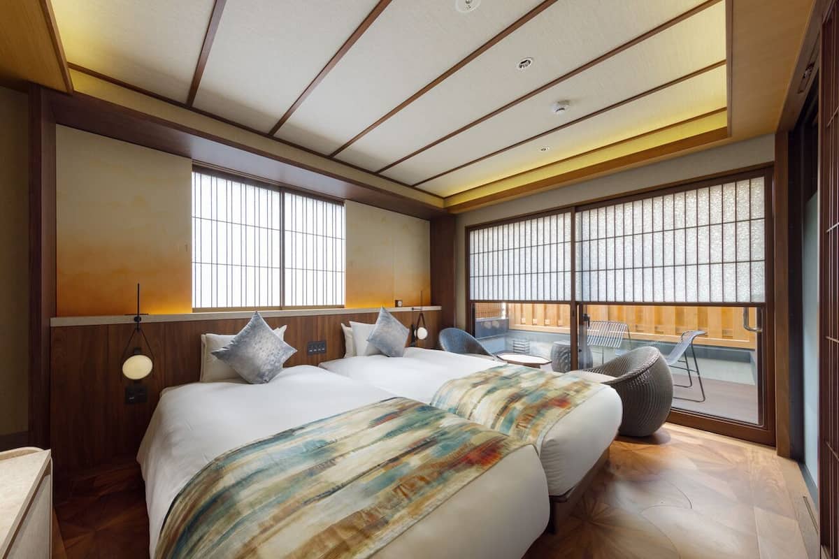 A hotel room with two beds, large windows, a view of the outside, and a wooden ceiling.