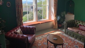 A room with a large window, a red leather sofa, a green armchair, a small table, and a patterned rug.