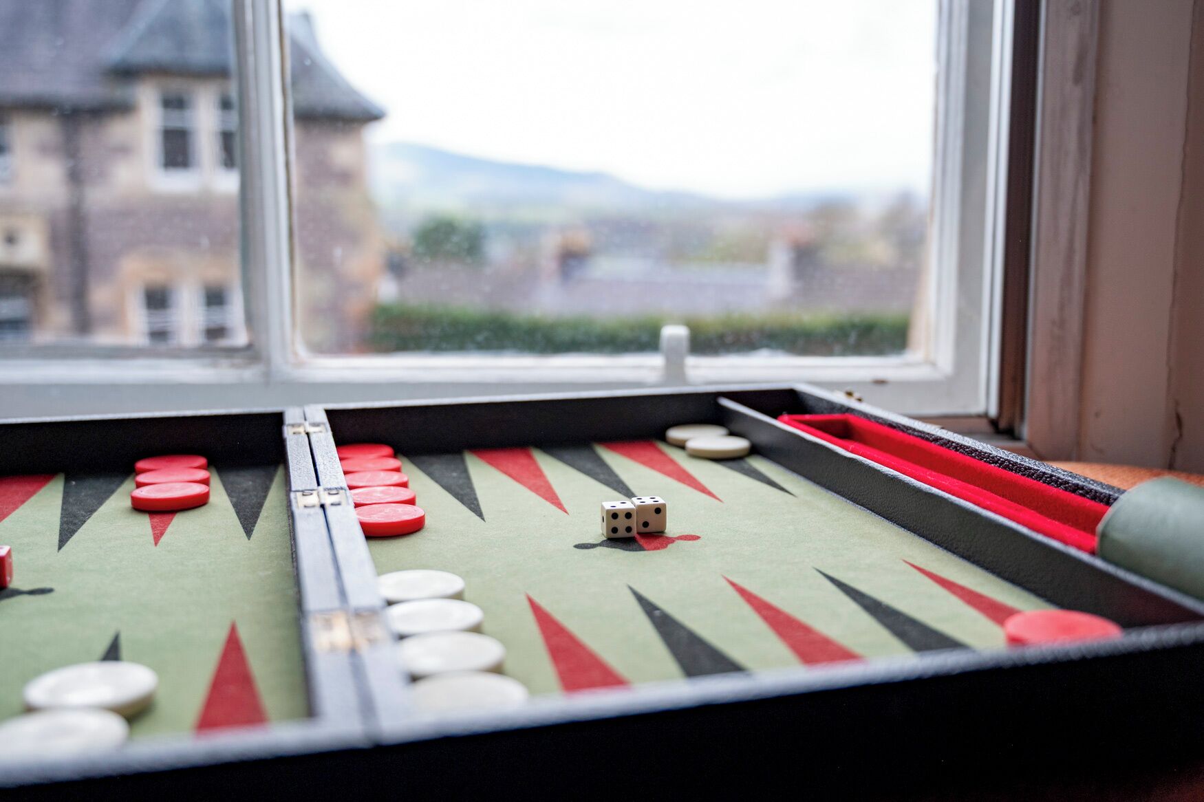 A backgammon board with dice and checkers, viewed through a window overlooking a building.