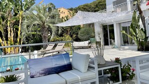 Zona junto a la piscina con mobiliario exterior blanco, una piscina y un edificio de diseño moderno al fondo.