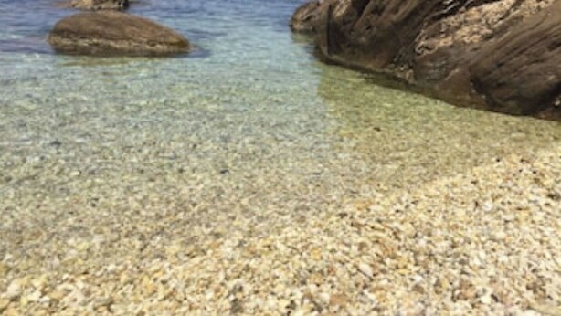 Una playa despejada con rocas visibles y barcos.