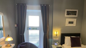 A hotel room with a bed, a chair, a nightstand, a lamp, and a window with curtains. - Cornerways Guest House (Carlisle)