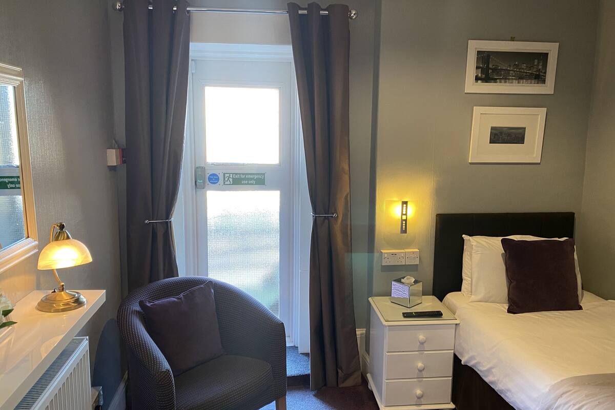 A hotel room with a bed, a chair, a nightstand, a lamp, and a window with curtains.