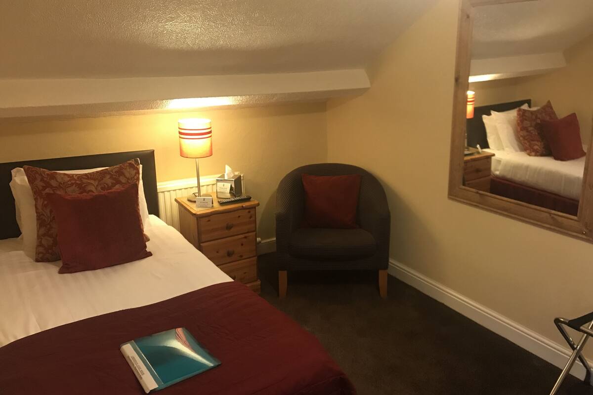 A hotel room with a bed, a chair, a nightstand, and a bedside table.