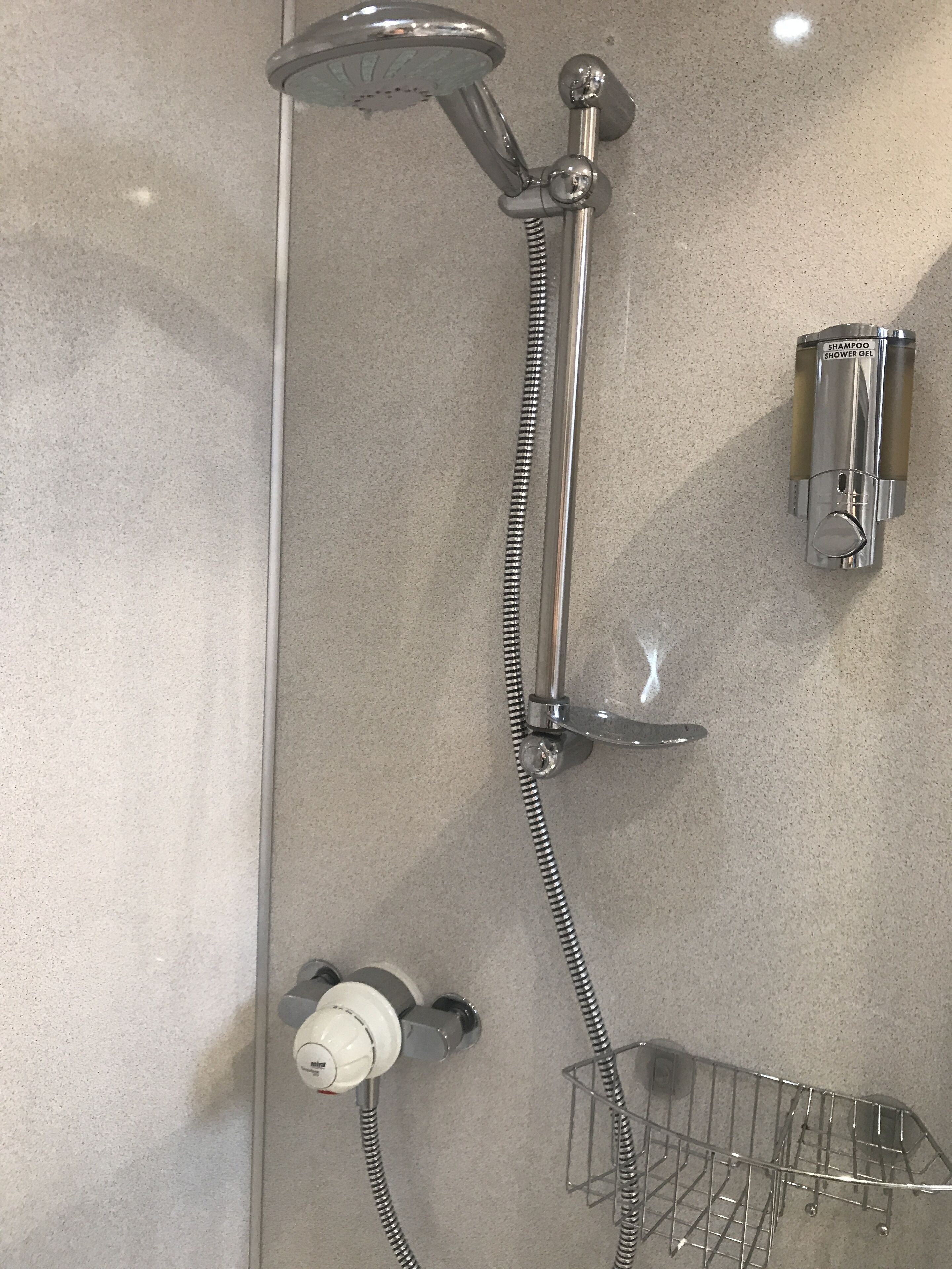 A shower with a handheld showerhead, a wall-mounted shampoo dispenser, and a towel rack.