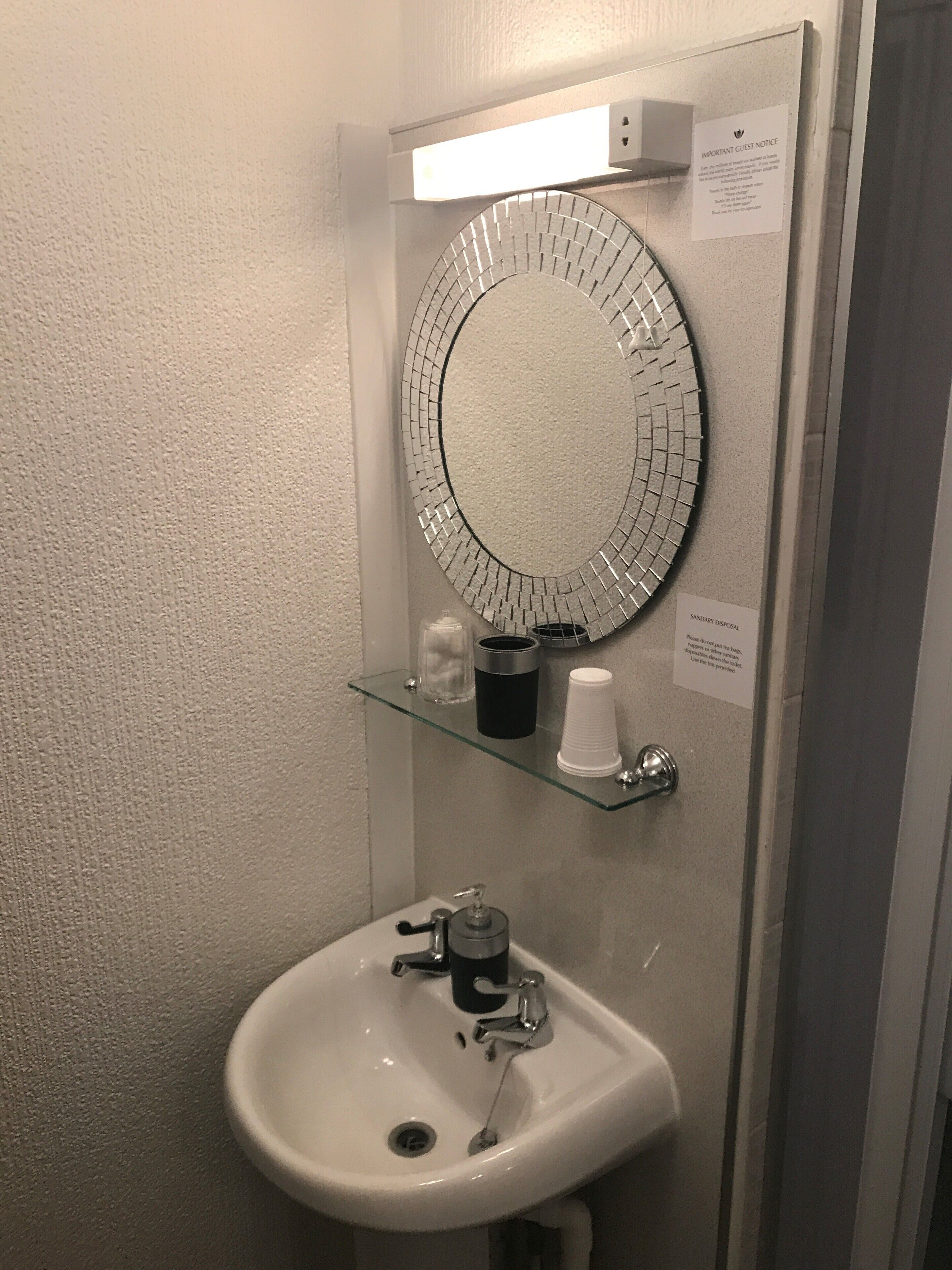 A bathroom with a white sink, a mirror, and a glass shelf with toiletries.