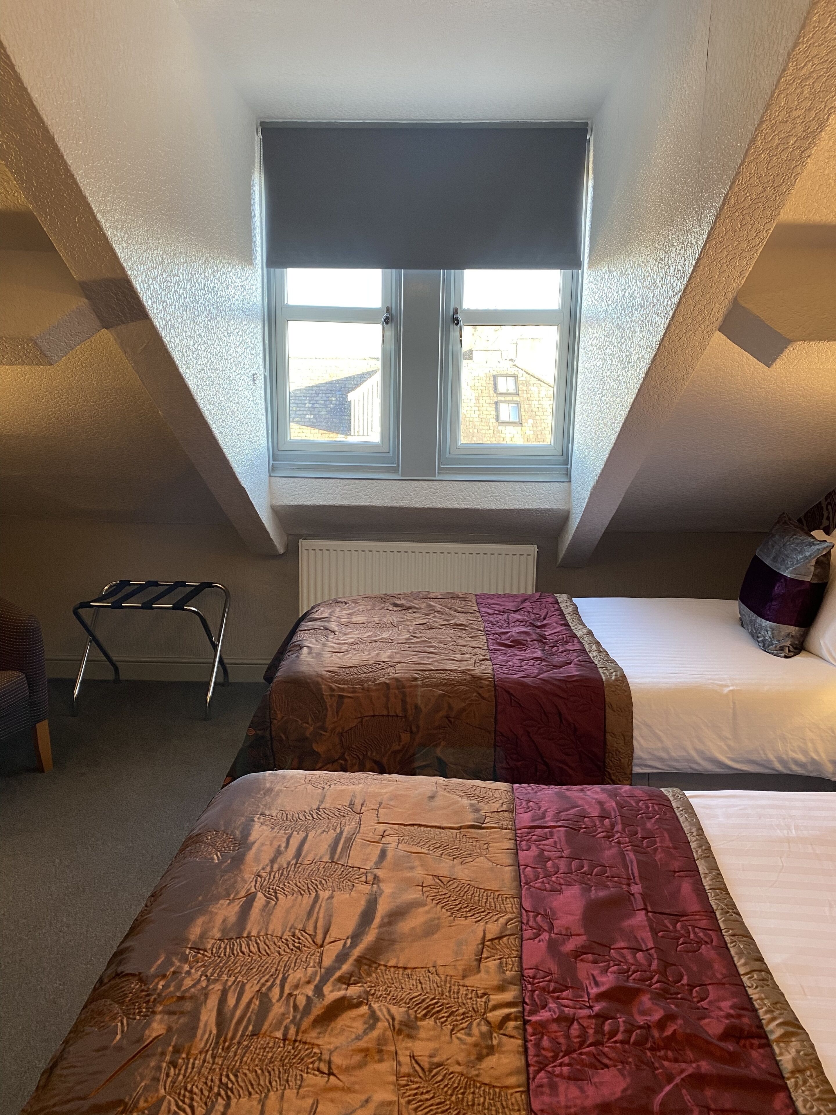 Un dormitorio con dos camas, un radiador, una ventana y una silla.