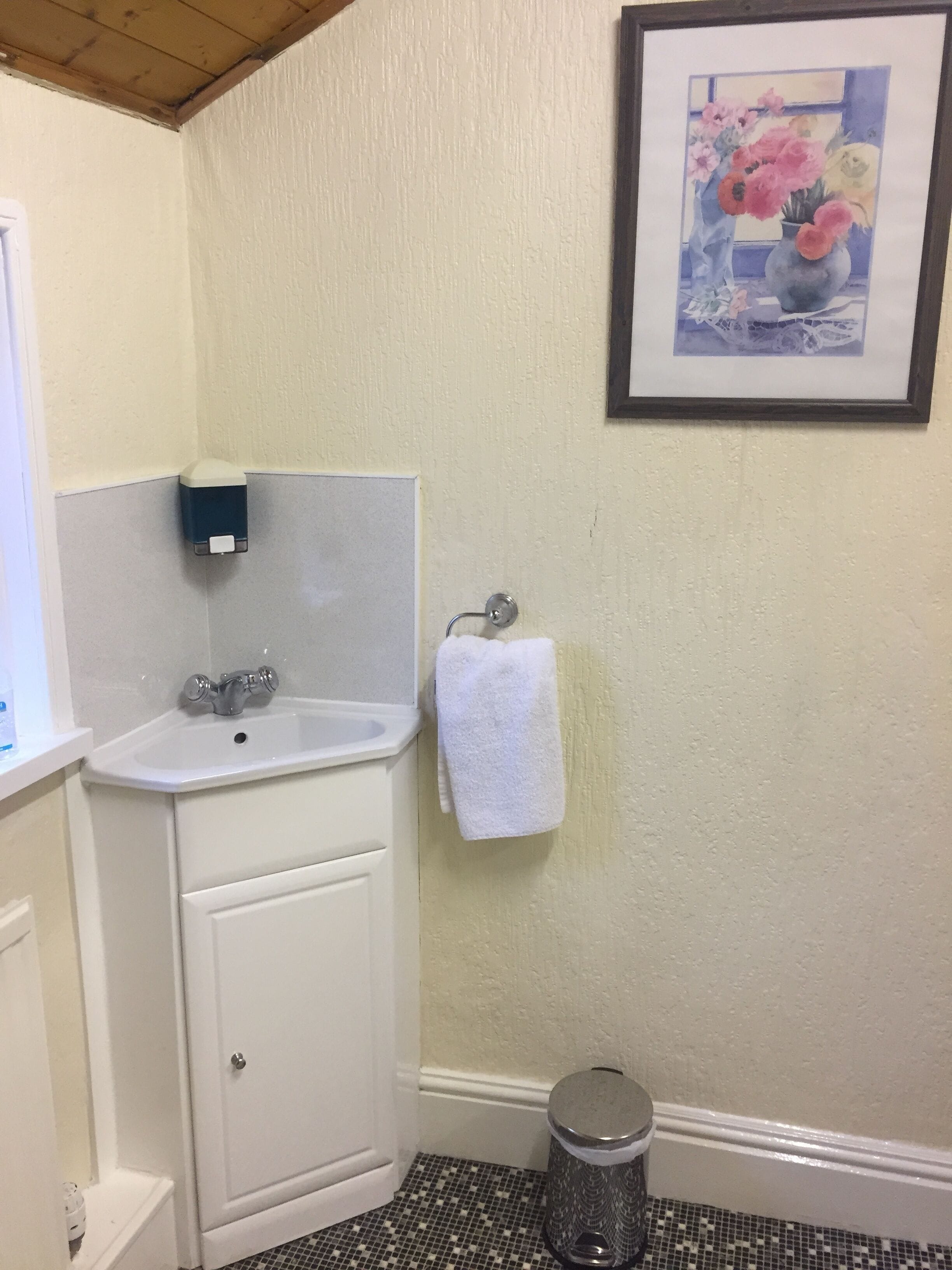A bathroom with a white sink, a framed painting of flowers, a white towel, and a trash can.