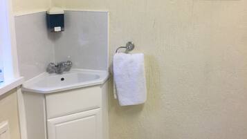 A bathroom with a white sink, a framed painting of flowers, a white towel, and a trash can.