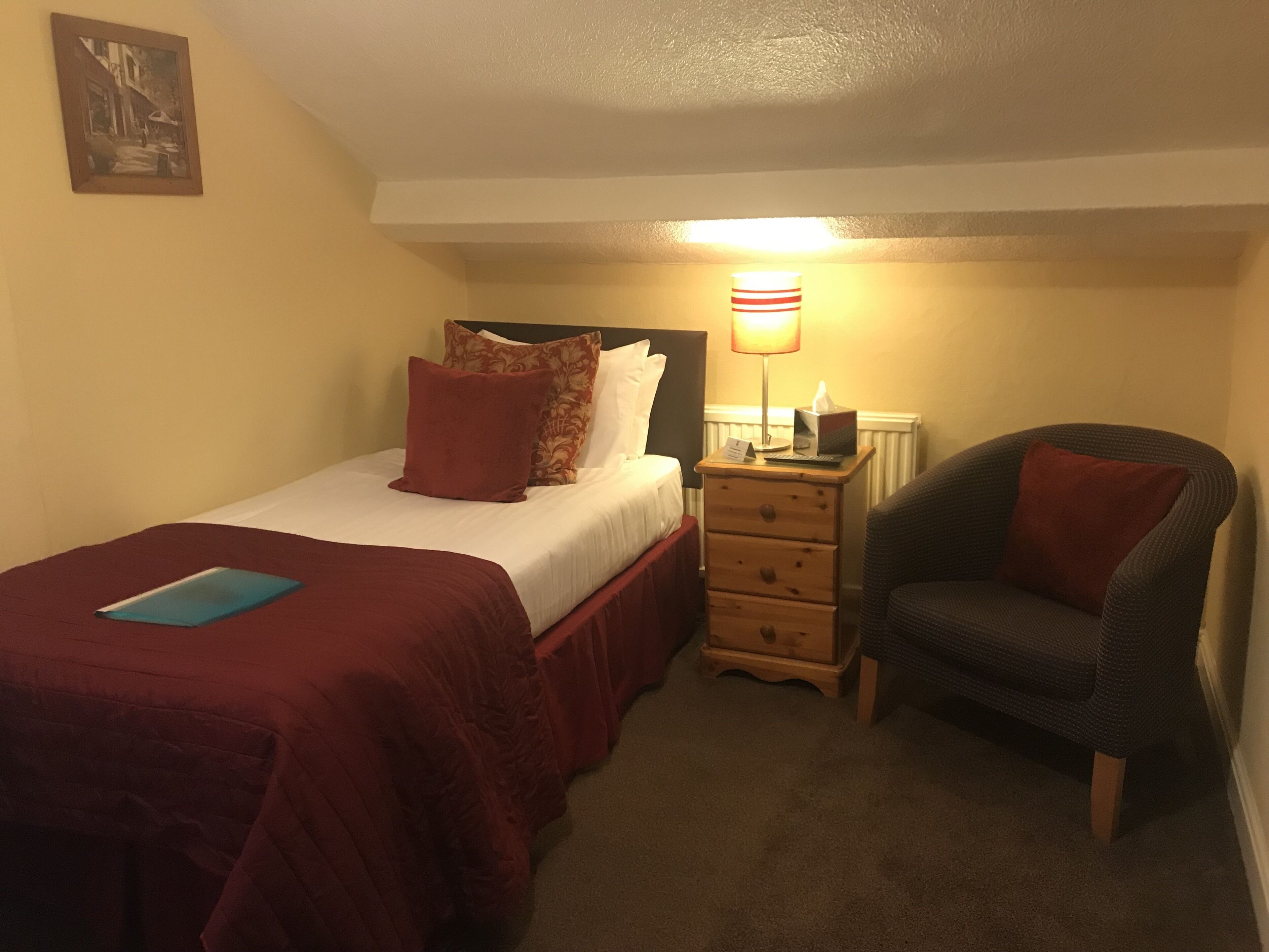 Un dormitorio con cama, mesita de noche, silla y lámpara.