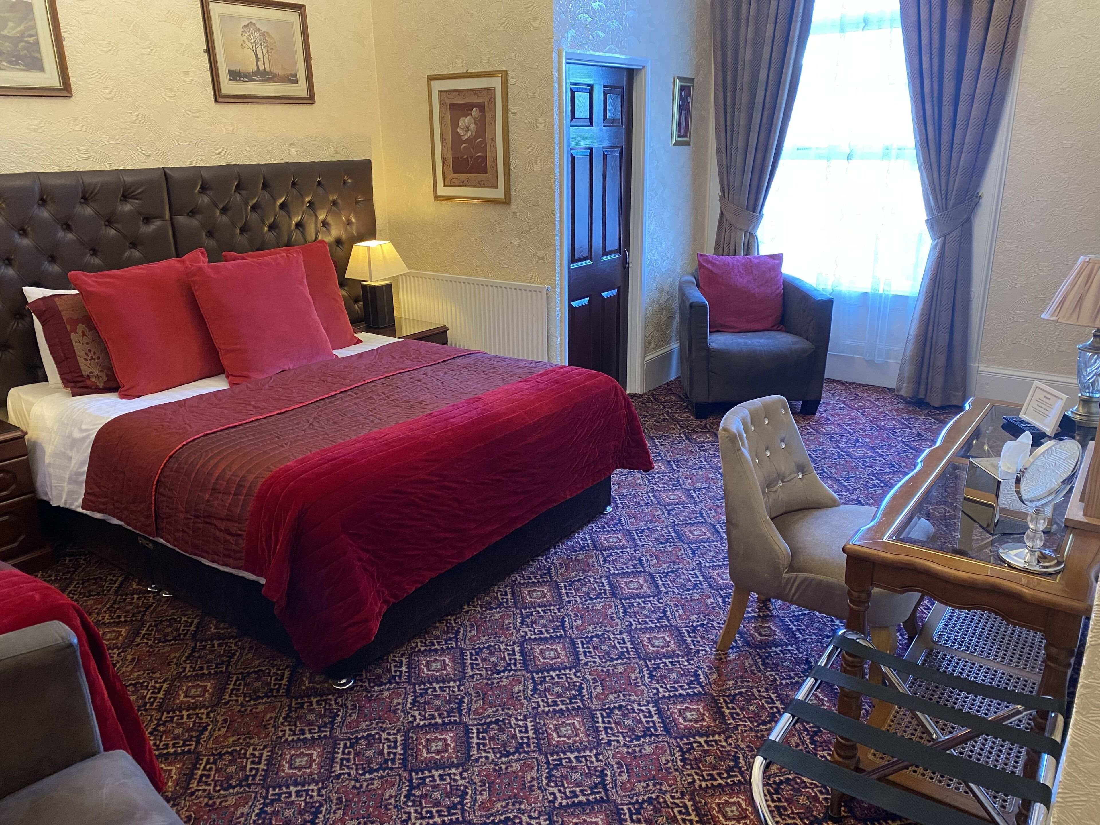 A hotel room with a large bed, a chair, a small table with a mirror, and a patterned carpet.