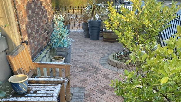 A brick patio with a wooden bench and table, surrounded by potted plants and a metal fence. - Cornerways Guest House (Carlisle)