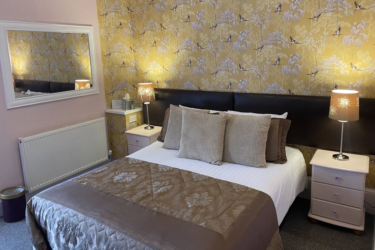 A neatly made bed with a floral bedspread, a headboard, and two bedside lamps.