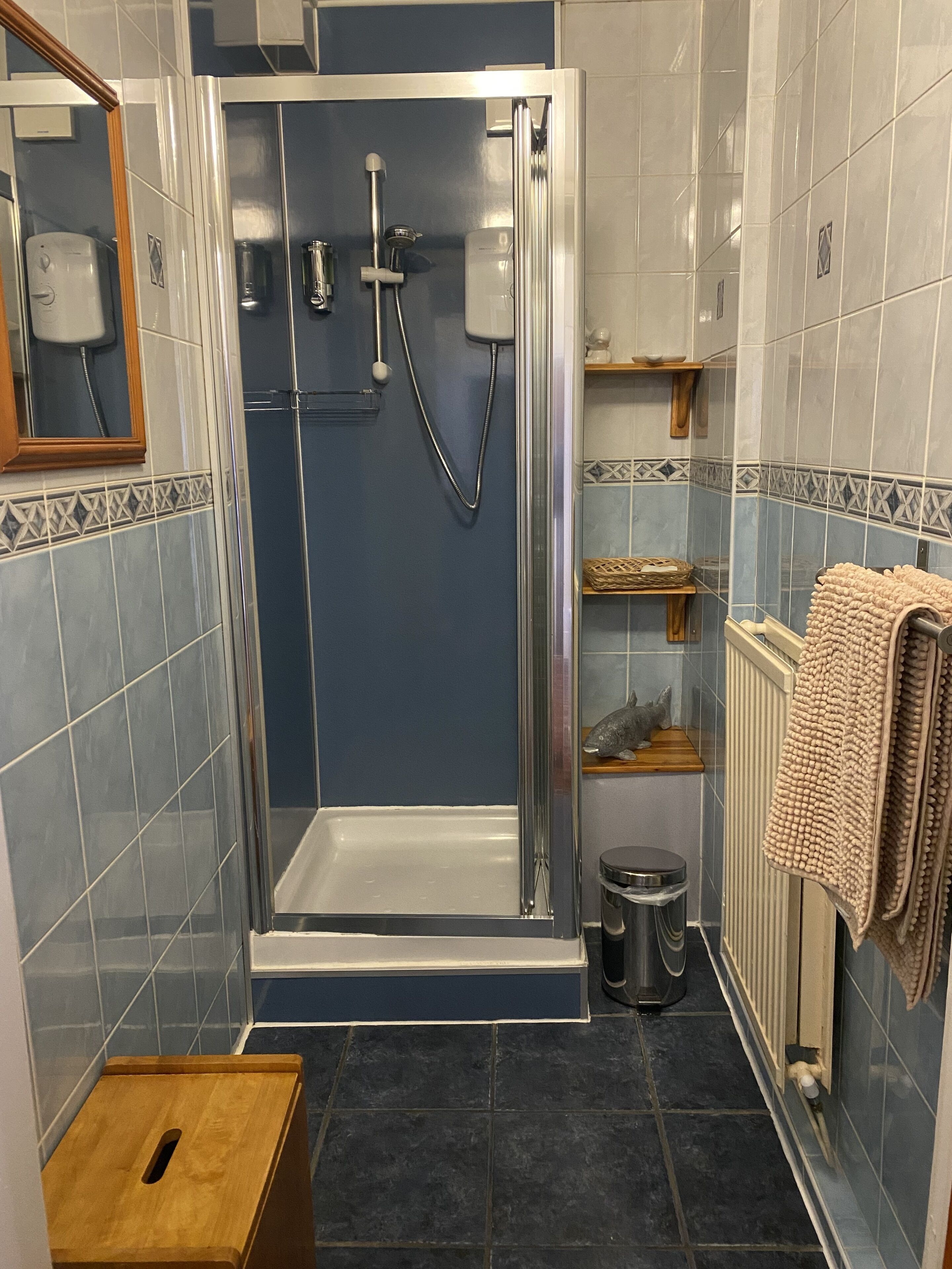 A bathroom with a glass-enclosed shower, a wooden stool, a radiator, and a towel rack.