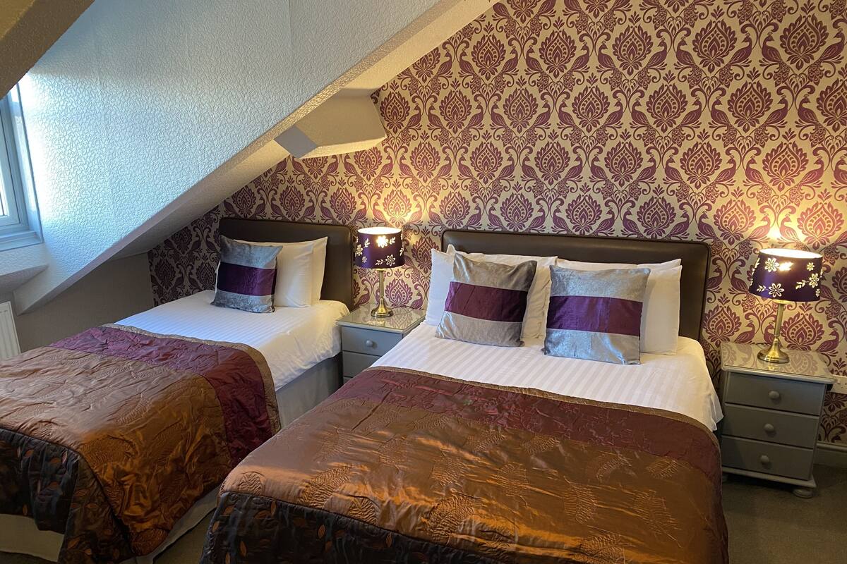 A bedroom with two beds, patterned wallpaper, and bedside lamps.