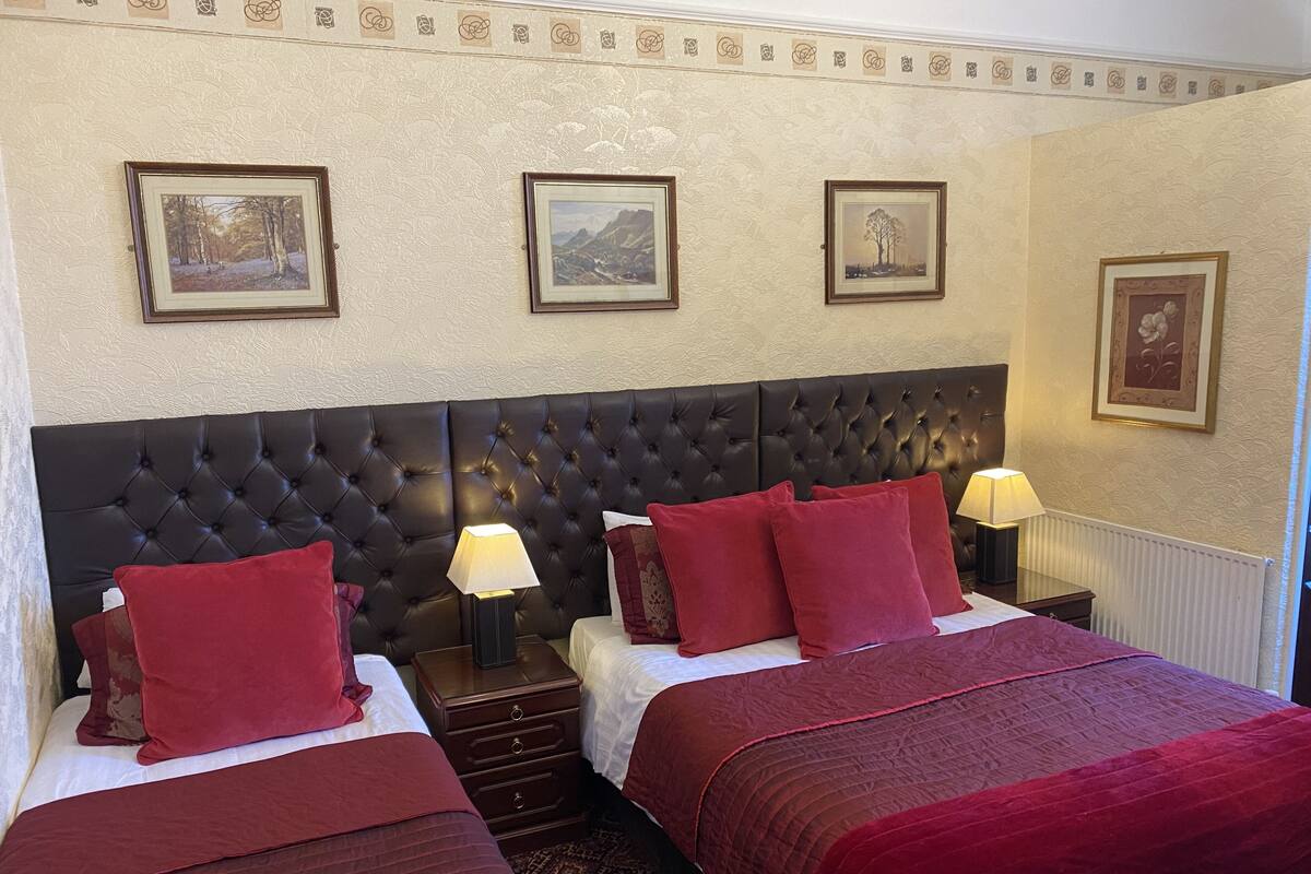 A hotel room with two beds, a large tufted headboard, and three framed pictures on the wall.