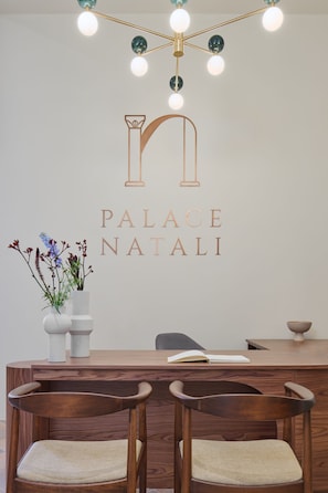 A reception desk with a logo for "Palace Natali," a vase with flowers, and two wooden chairs. - Palace Natali (Dubrovnik)