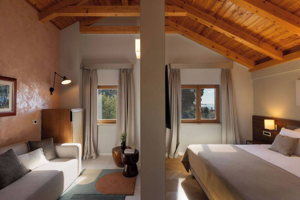 Une chambre d’hôtel avec un plafond en bois, deux lits, un canapé, une petite table, une lampe et une vue sur l’extérieur.