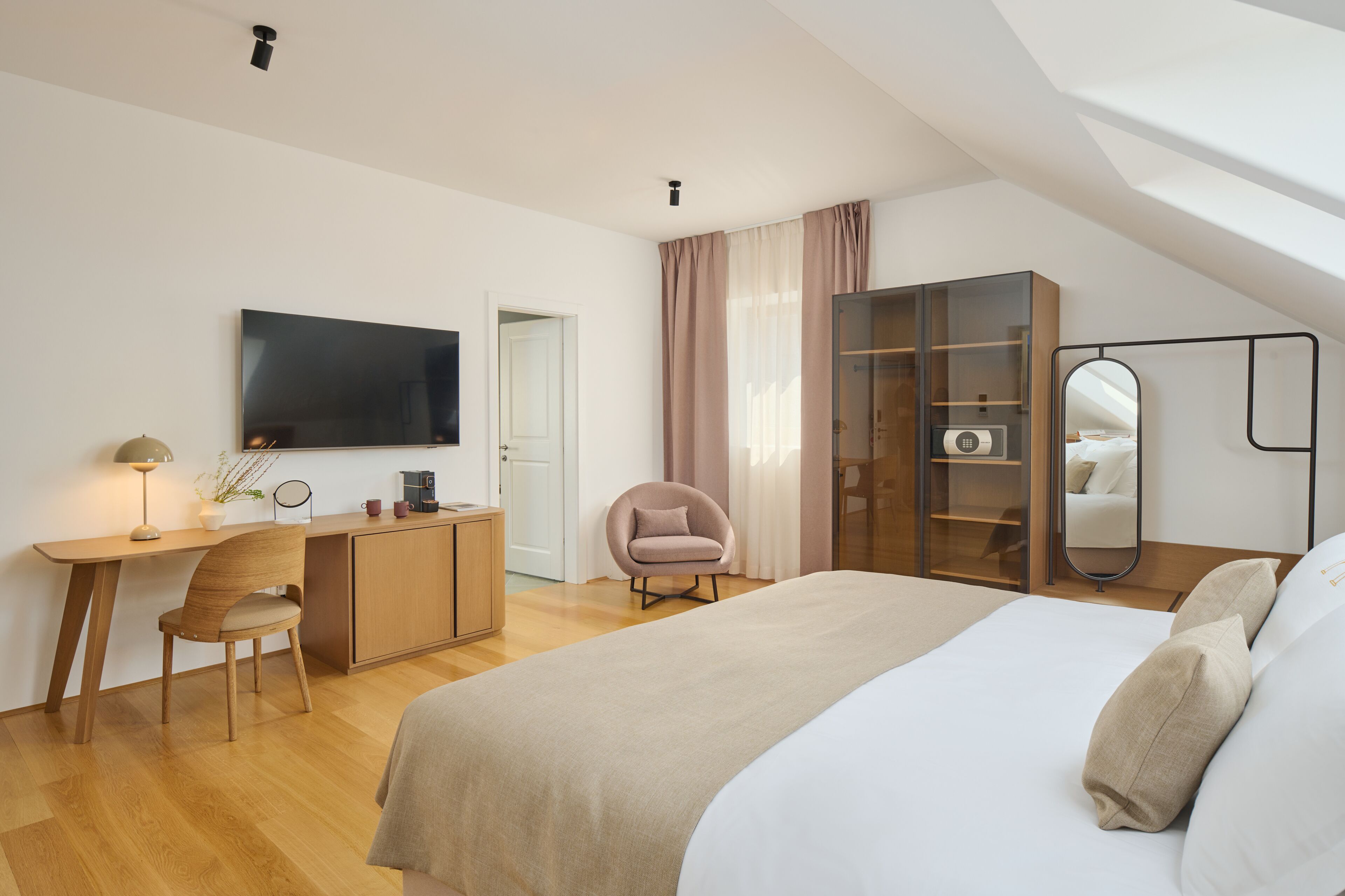 Un dormitorio moderno con una cama grande, un escritorio con silla, un armario y un televisor en la pared.