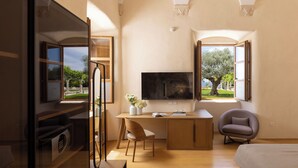 A modern bedroom with a large bed, a desk with a chair, a television, and two windows offering views of the outdoors. - Palace Natali (Dubrovnik)