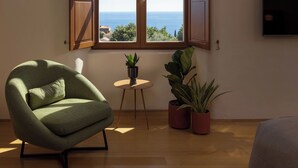 A room with a large window, a green armchair, a small table, and two potted plants. - Palace Natali (Dubrovnik)