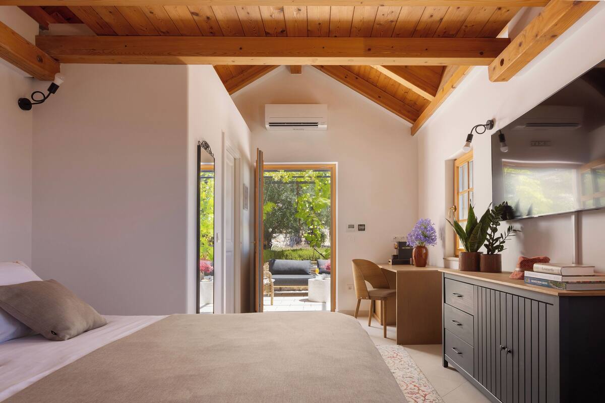 Une chambre à coucher avec un lit, un bureau et une chaise. Il y a une fenêtre qui donne sur un paysage verdoyant.