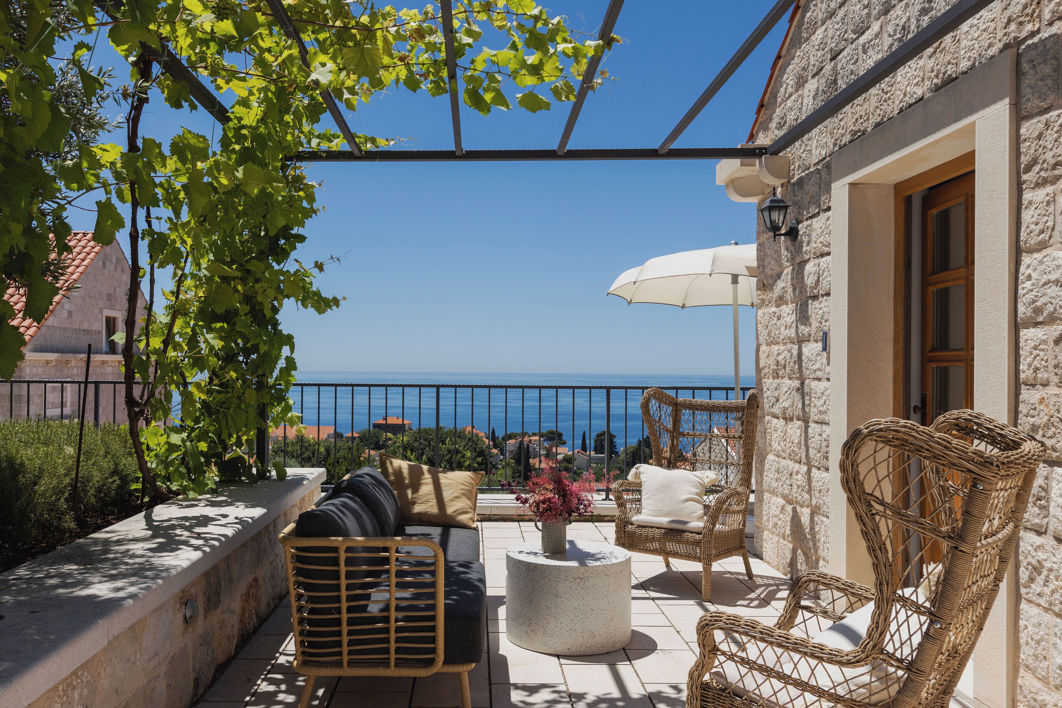 A terrace with wicker furniture, a stone wall, and a view of the sea.