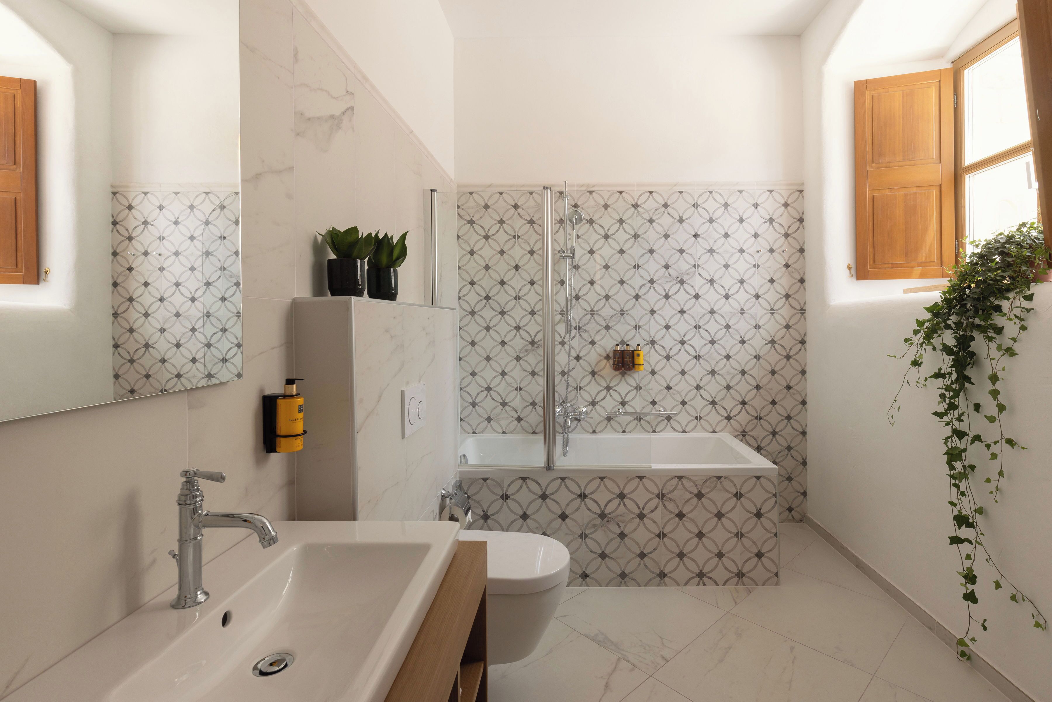 Un baño con lavabo, inodoro y ducha. Hay plantas y un espejo en la pared.