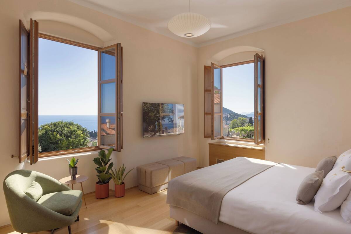 Une chambre à coucher avec un lit, une chaise, une petite table sur laquelle se trouve une plante, et un tableau accroché au mur.