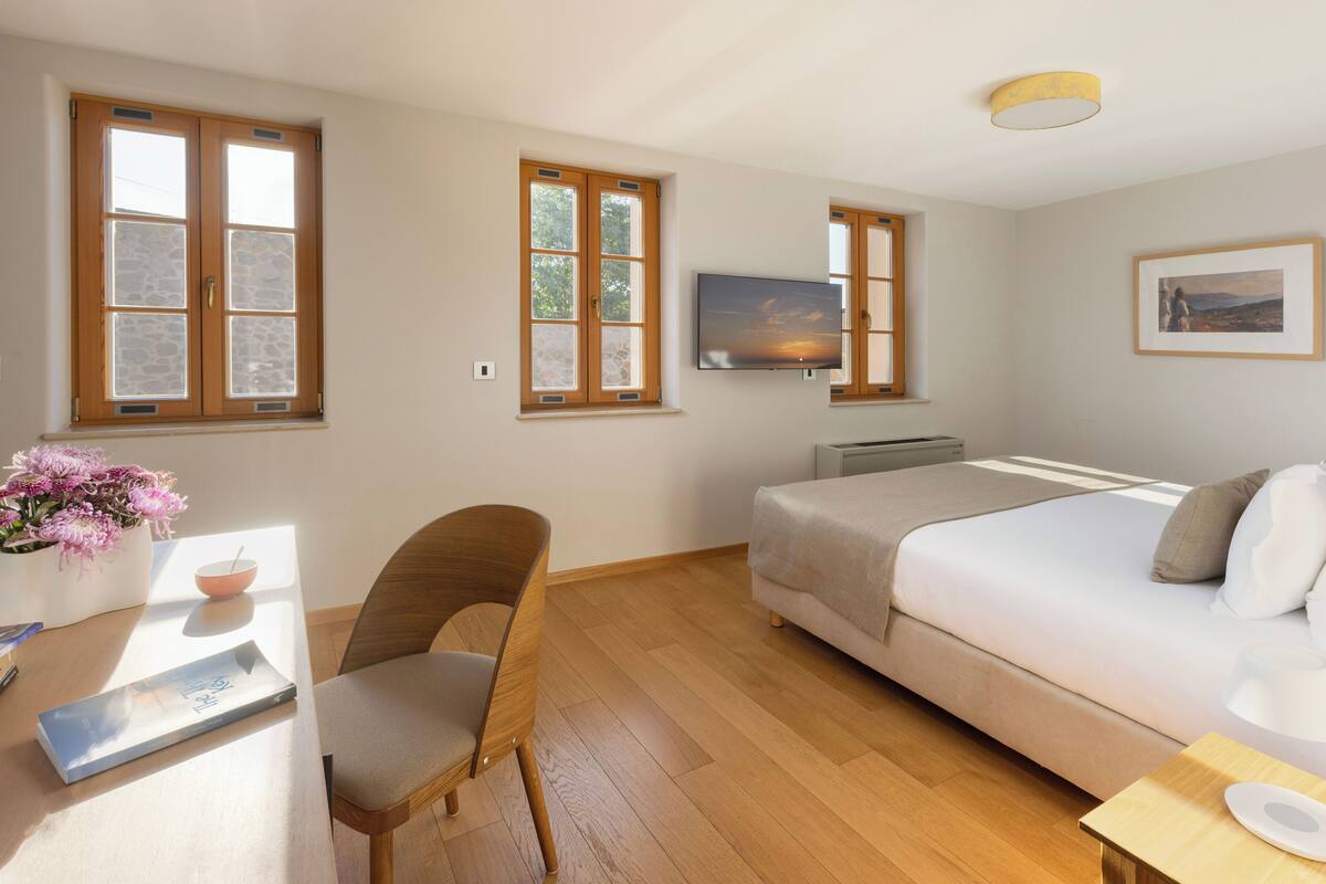 Une chambre à coucher avec un lit, un bureau avec une chaise, une télévision et une fenêtre donnant sur un paysage agréable.
