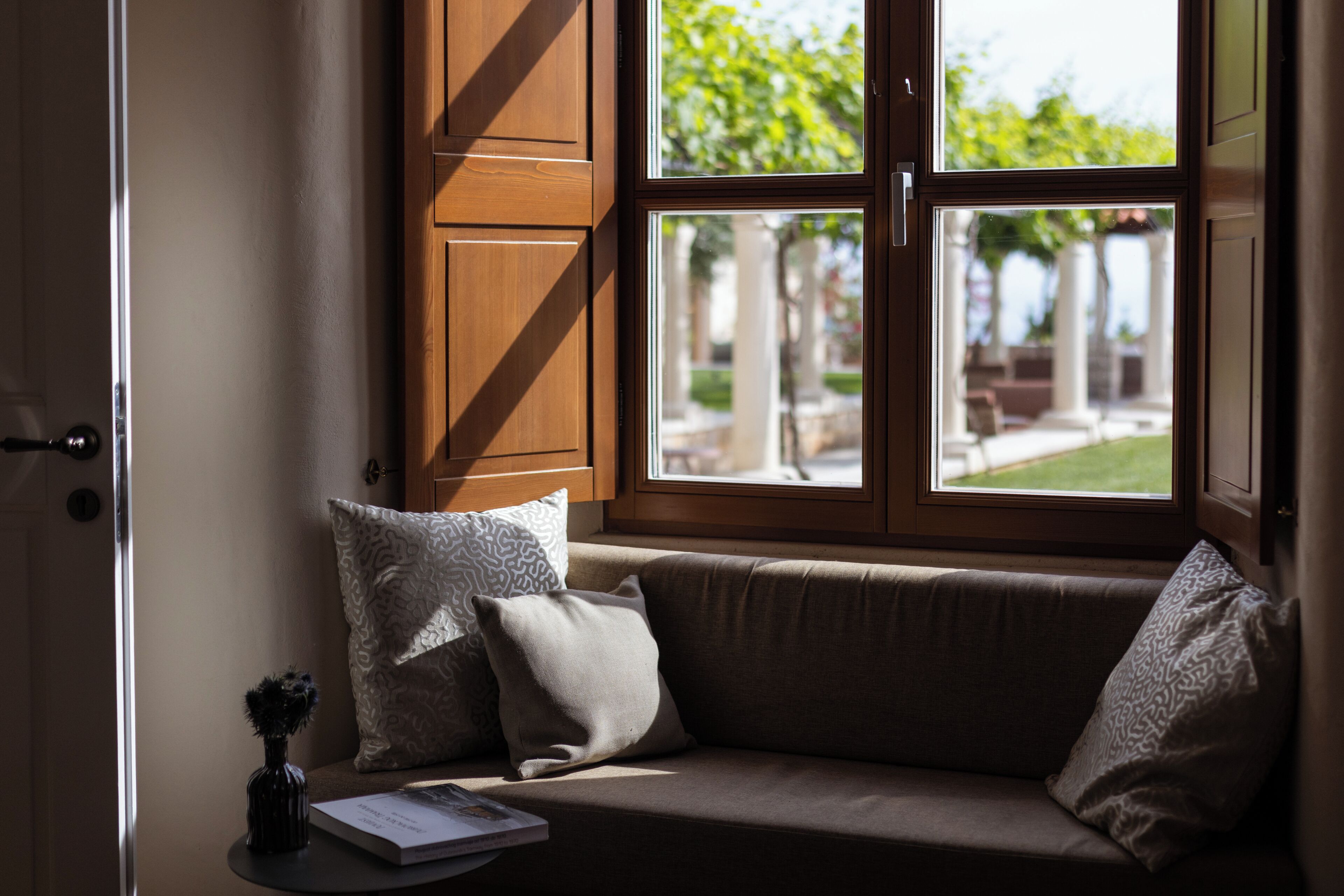 Una habitación con ventana, un sofá y una mesita con un jarrón y un libro.