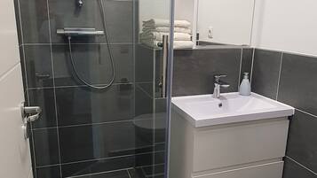 Un baño moderno con ducha de vidrio, lavamanos blanco y un espejo sobre él.