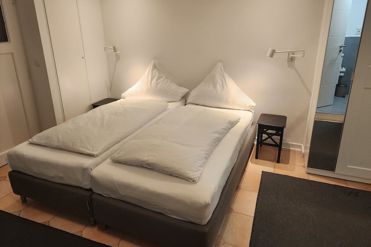 A double bed with white bedding, a small bedside table, and a dark-colored bench.