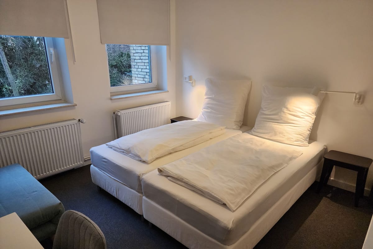 A room with a bed, a desk, and two windows.