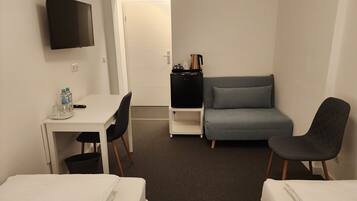 A hotel room with a bed, a desk with a chair, a sofa, and a TV.