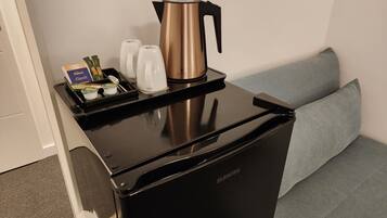 A compact, black coffee machine with a stainless steel pot and a tray with two white cups and a box of coffee pods.