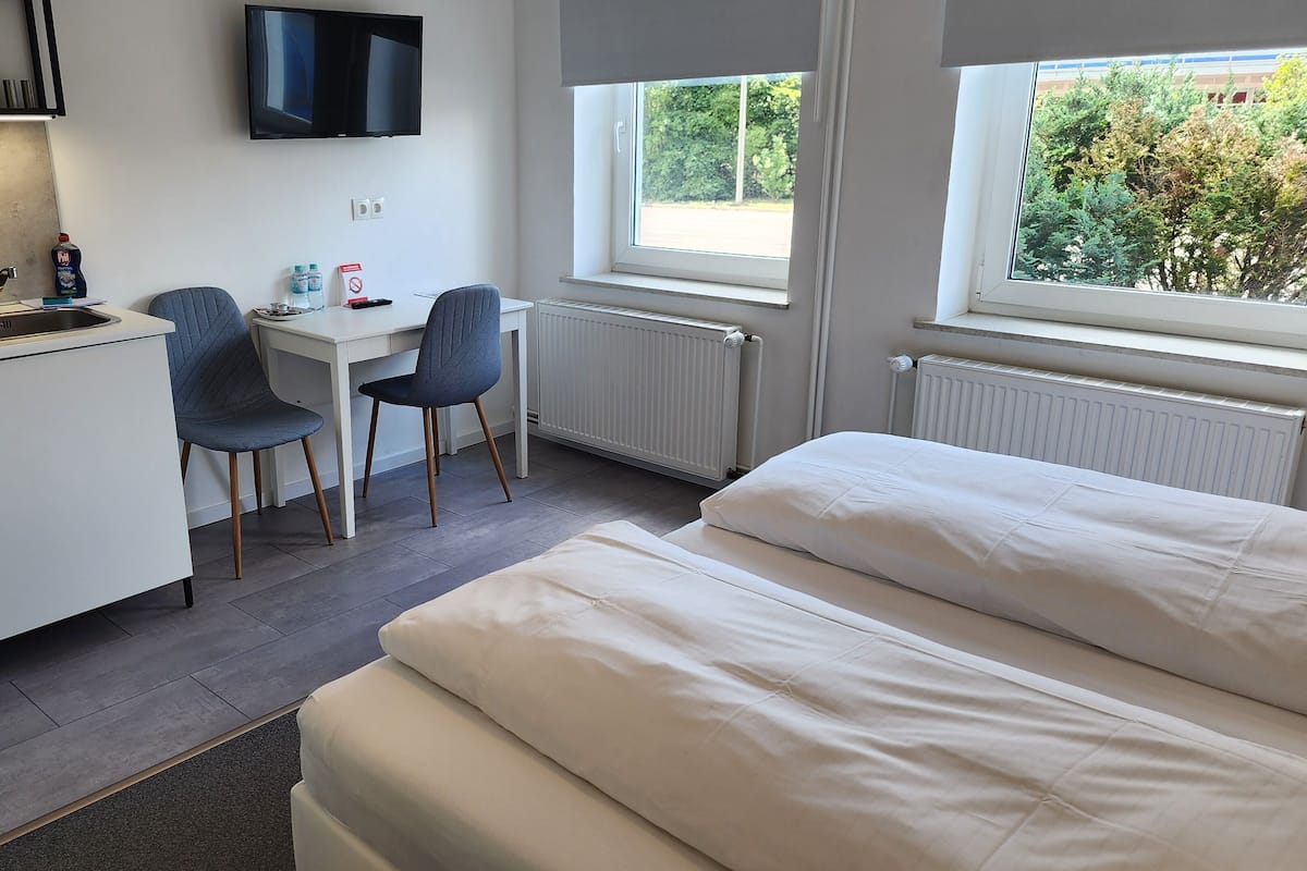 A compact hotel room with a kitchenette, a bed, a desk with two chairs, and a TV.