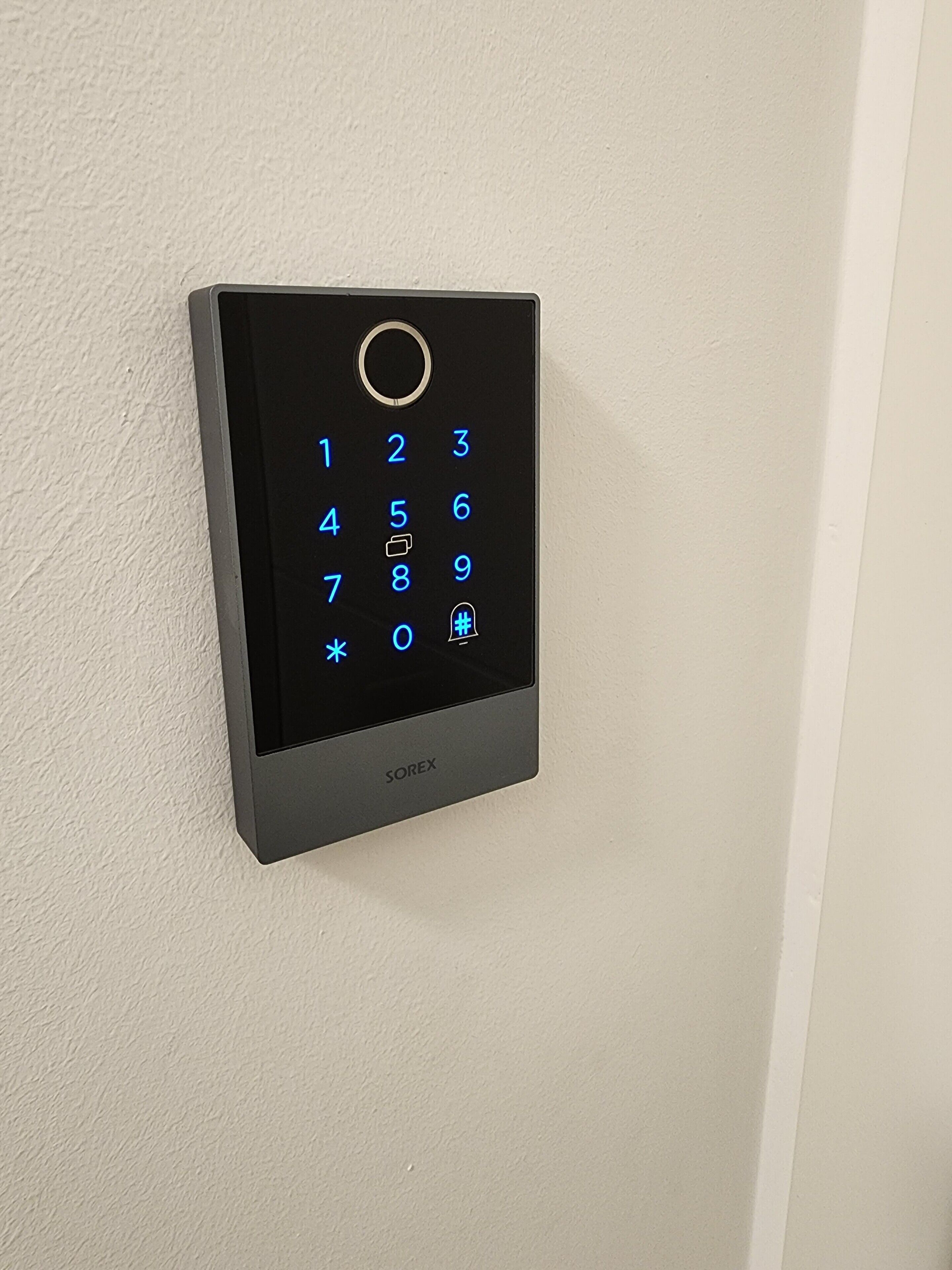 A wall-mounted electronic keypad with a numeric keypad and a circular button at the top.