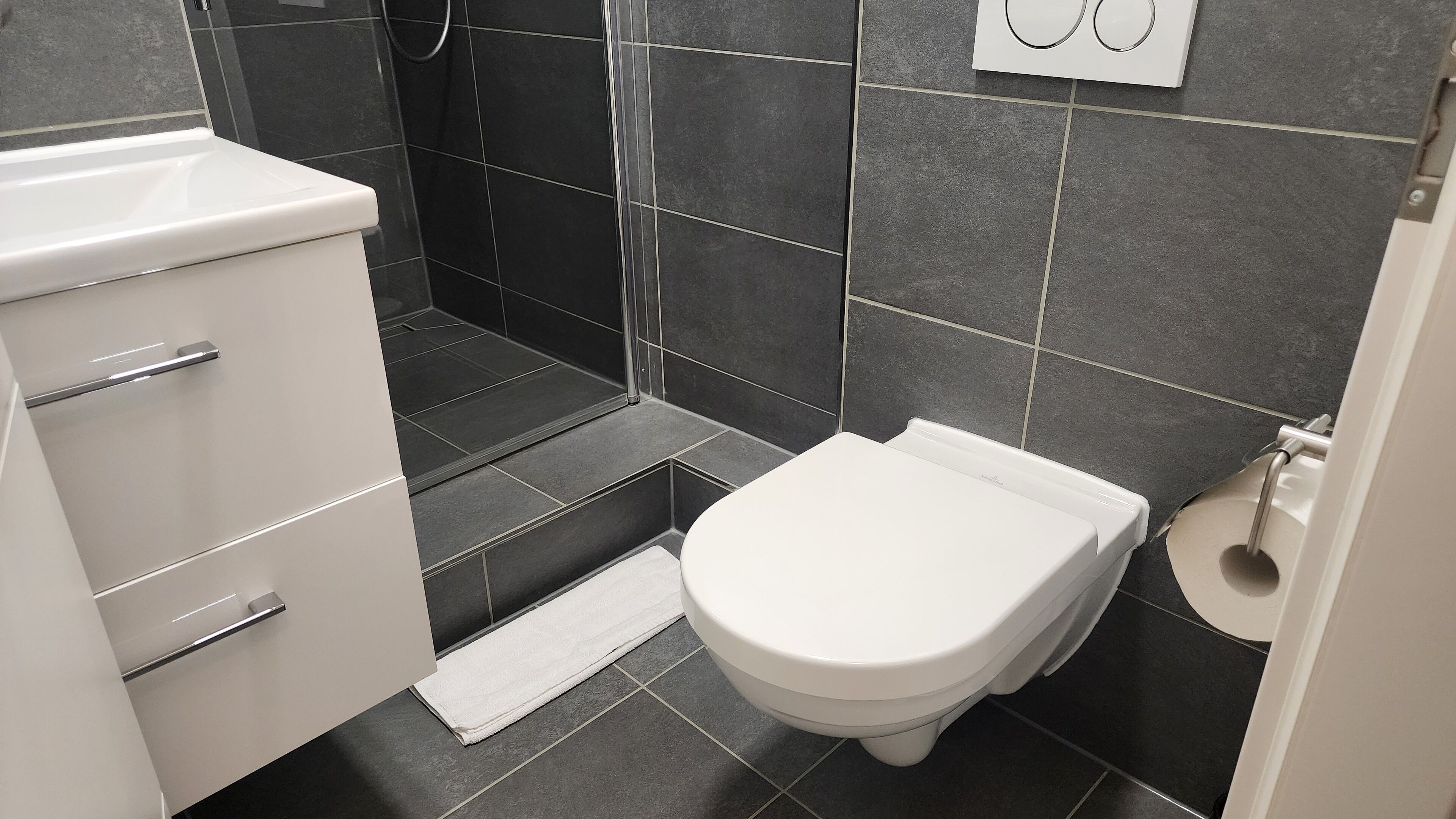 A modern bathroom with a white toilet, a white sink, and a shower area.