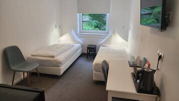 Une petite chambre propre, avec deux lits simples, un bureau avec une chaise, une petite table et une fenêtre donnant sur un paysage verdoyant.