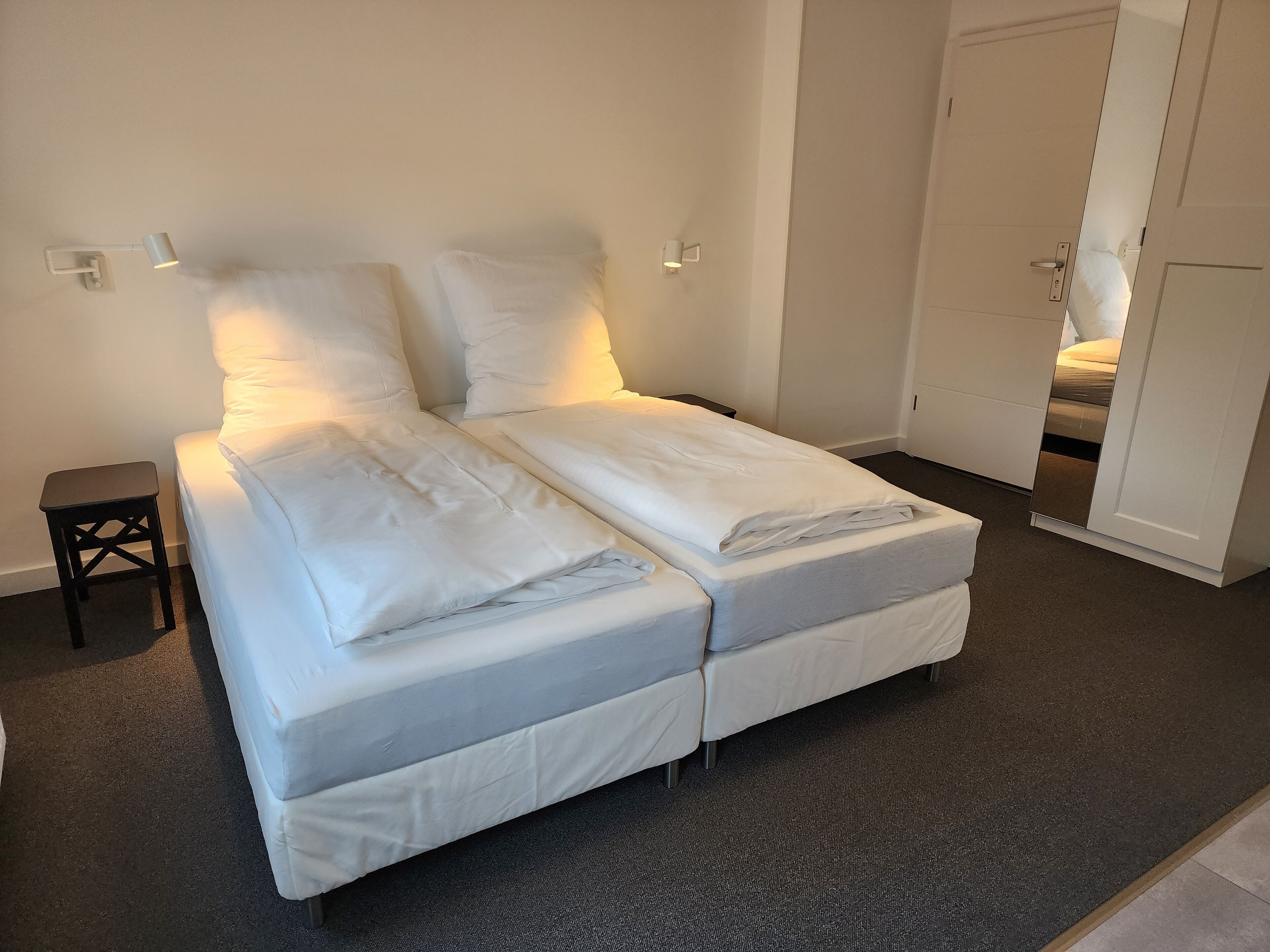 A neatly made double bed with white bedding, a small bedside table, and a wall-mounted light fixture.