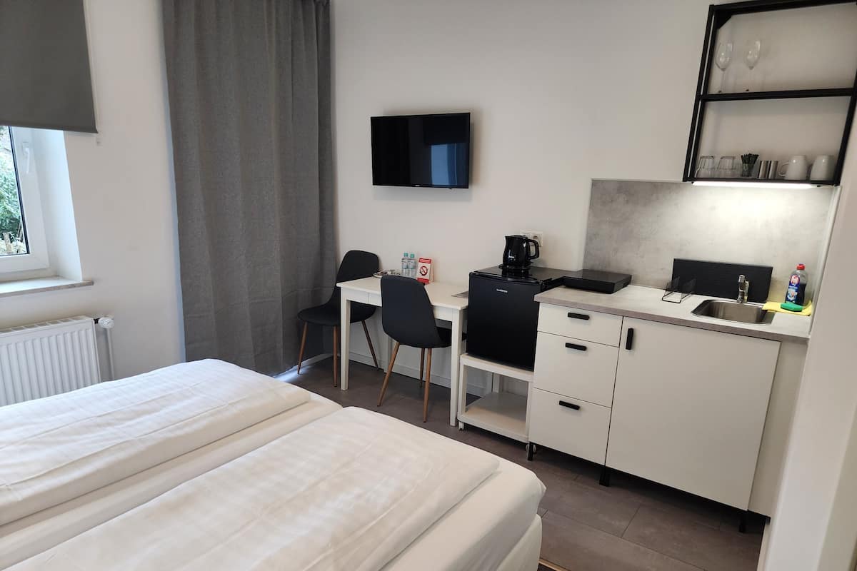 A hotel room with a bed, a desk with a chair, a television, a coffee maker, a sink, and a shelf with glasses and cups.