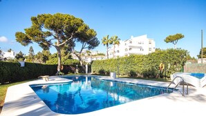 Ein Pool mit gewölbter Kante, umgeben von einer weißen Terrasse und einer Hecke.