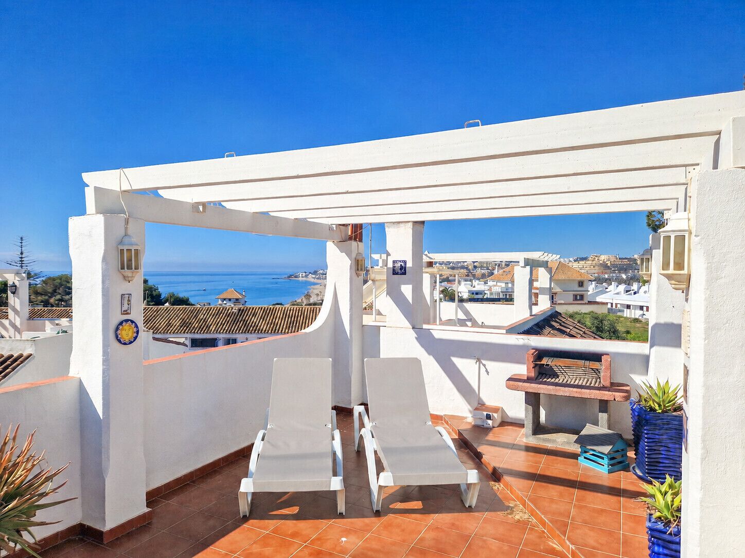 A rooftop terrace with two lounge chairs, a barbecue area, and a view of the sea and cityscape.