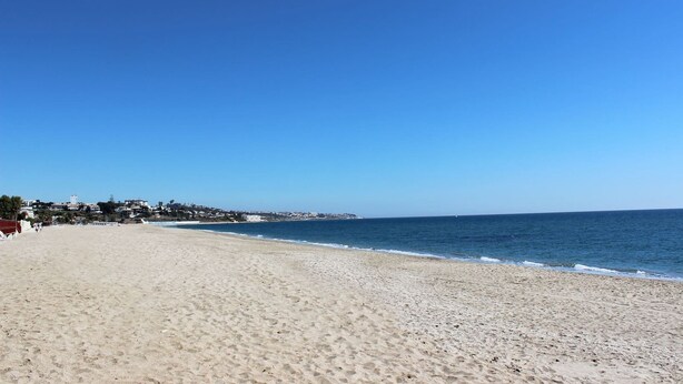 Ein weiter Sandstrand mit blauem Himmel und ruhiger See.