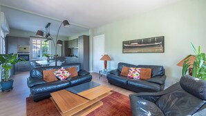 Een moderne woonkamer met leren banken, een salontafel en een eetgedeelte, met een keuken op de achtergrond.